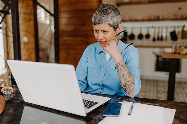 middle-aged female with short hair in a blue button up shirt looking at their laptop